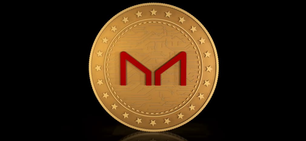 A golden coin with the Maker (MKR) logo embossed in the center