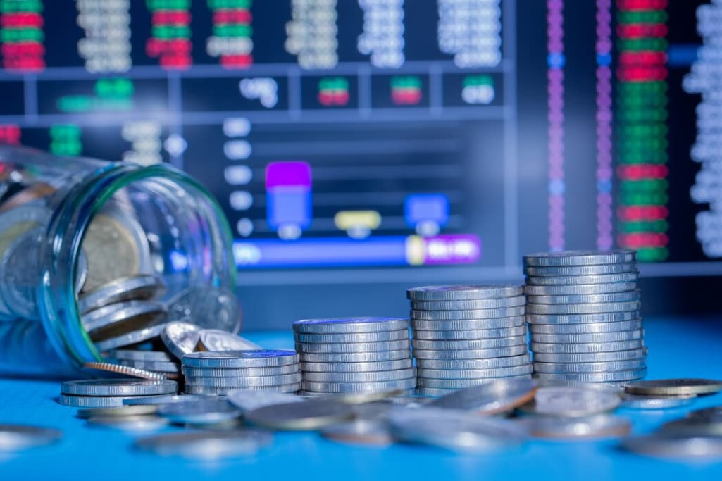 Stacked coins in focus against a blurred stock market screen background